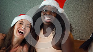 Young girls of Europe, Asia and Africa in red New Year`s clothes and hats sit on the bed at the Christmas tree, give gifts and