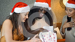 Young girls of Europe, Asia and Africa in red New Year`s clothes and hats sit on the bed at the Christmas tree, give gifts and