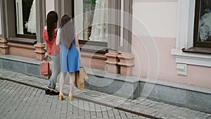 Young girls friends standing near shop window with wedding dresses and discuss. slow mo