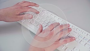 Young girls' hands operate a white computer keyboard.