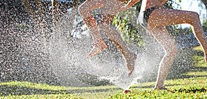 Young girls playing jumping in a garden water lawn sprinkler