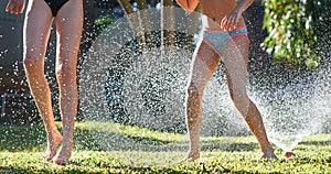 Young girls playing jumping in a garden water lawn sprinkler