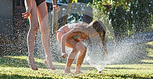 Young girls playing jumping in a garden water lawn sprinkler