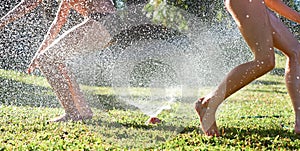 Young girls playing jumping in a garden water lawn sprinkler