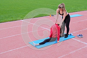 Young girls in the red sweater in nature doing stretching. Coach stretches partner on the twine. Classes in the park. Health.