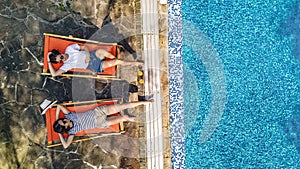 Young girls relax near swimming pool in sunbed deckchairs, women friends relax in hotel resort, aerial drone view from above photo