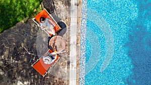 Young girls relax near swimming pool in sunbed deckchairs, women friends relax on tropical vacation in hotel resort, aerial view