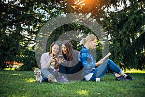 Young girls relax in the park on green grass. Students spend their free time in nature, read books, communicate in social networks