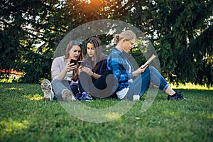 Young girls relax in the park on green grass. Students spend their free time in nature, read books, communicate in social networks