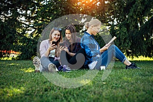 Young girls relax in the park on green grass. Students spend their free time in nature, read books, communicate in social networks