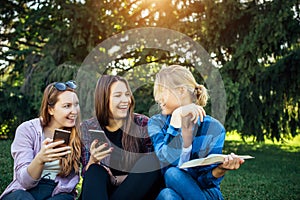 Young girls relax in the park among green trees, close-up. Students spend their free time in nature, read books, communicate