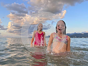 Young girls swimming in the wave with splash. Happy children, summer vacation concept