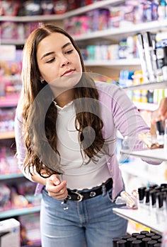 Young glad woman choosing lipsticks on stand in cosmetics store