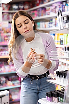 Young glad woman choosing lipsticks on stand in cosmetics store