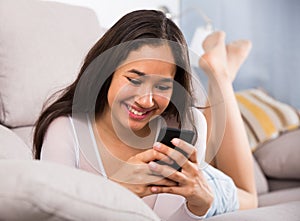 Young glad woman lying with mobile