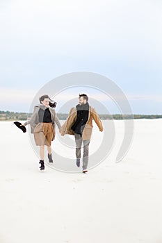 Young gladden couple walking on snow and holding hands, winter background.