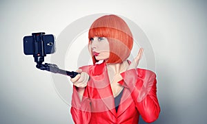 Young glamor girl in red making selfie with a stick