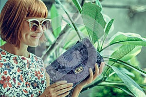 Young glamour woman wearing flower dress posing with luxury handmade snakeskin python handbag. Beautiful stylish girl