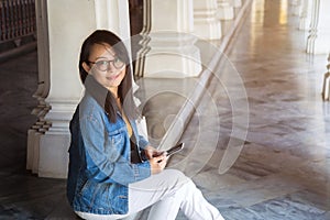 Young glasses Asian woman in jeans jacket sitting on pavilion