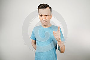 Young gloomy threaten man with a finger, dressed in a blue t-shirt on a light background. Close up portrait