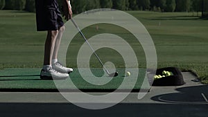 Young golfer practices his golf swing on driving range, view from side