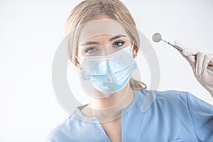 Young good looking female dentist on a white isolated background holding a stainless steel dental mirror