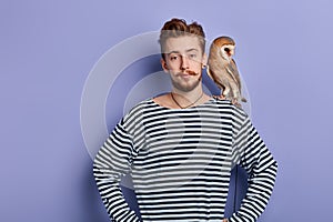 Young good looking man holds a predatory tamed owl on his shoulder photo