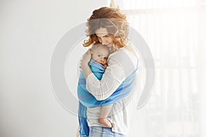 Young good-looking mother snuggles and calming her newborn son who feeling scared after long sleep interrupted by loud