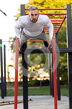 Young good looking muscular man doing pushups outdoors on parallel bars