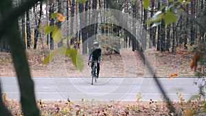 Young good-looking professional cyclist in cycling apparel and helmet trying to stand in track on road bike. Stylish young male tr