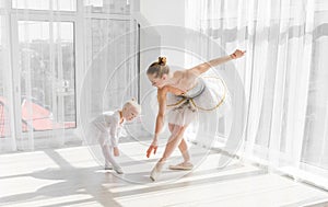 Young gorgeous ballerina with her little daughter dancing in studio