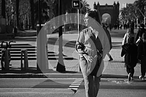 Young gorgeous elegant woman with pouch crossing the road along street. Black and white photo