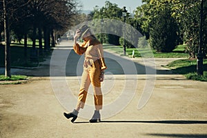 Young gorgeous woman in bright overalls and hat walking along park. Posh model posing outdoor