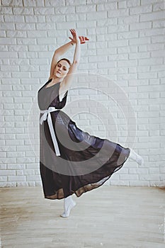 Young and graceful ballerina in pointe shoes and black dress dances in the studio. Choreography and dancing classes concept.