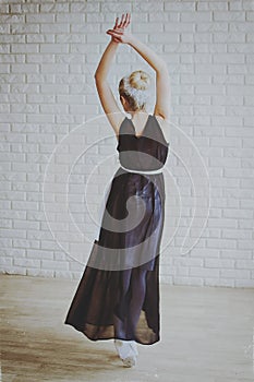 Young and graceful ballerina in pointe shoes and black dress dances in the studio. Choreography and dancing classes concept.