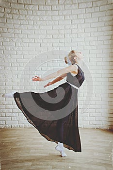 Young and graceful ballerina in pointe shoes and black dress dances in the studio. Choreography and dancing classes concept.