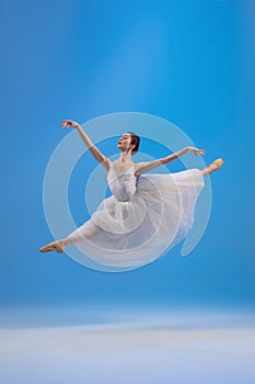 Young and graceful ballet dancer isolated on blue studio background. Art, motion, action, flexibility, inspiration
