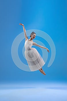 Young and graceful ballet dancer isolated on blue studio background. Art, motion, action, flexibility, inspiration