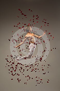 Young and graceful ballet dancer on studio background with rose petals. Art, motion, action, flexibility, inspiration