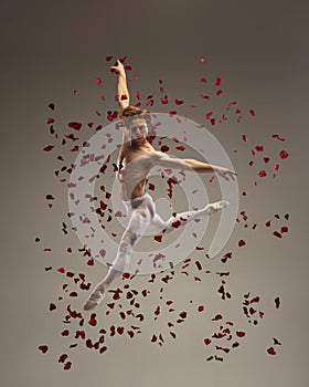 Young and graceful ballet dancer on studio background with rose petals. Art, motion, action, flexibility, inspiration