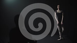 Young graceful woman ballerina in black dress slowly dancing in black studio - the jury looks at her