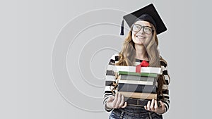 Young graduated student looking away and carrying books on gray background