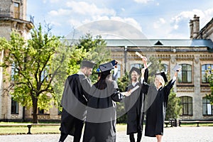 young graduated students with diplomas greeting each other