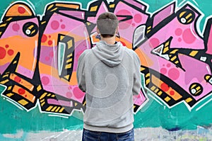 A young graffiti artist in a gray hoodie looks at the wall with