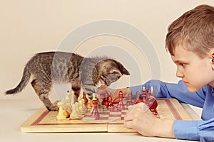 Young grandmaster with tabby kitten plays chess.