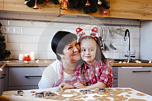 Young grandmother and granddaughter embrace in the kitchen while making cookies on Christmas Eve