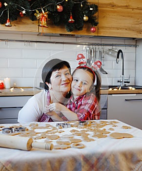 Young grandmother and granddaughter embrace in the kitchen while making cookies on Christmas Eve