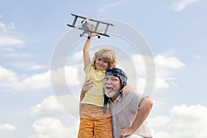 Young grandson and old grandfather playing with plane together on blue sky. Cute child with granddad playing outdoor