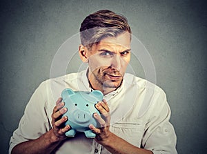 Young greedy stingy business man holding piggy bank photo