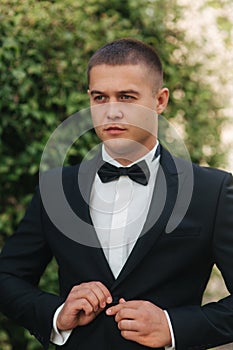 Young groom in suit otside. Handsome man in black suit. Model walking in the park